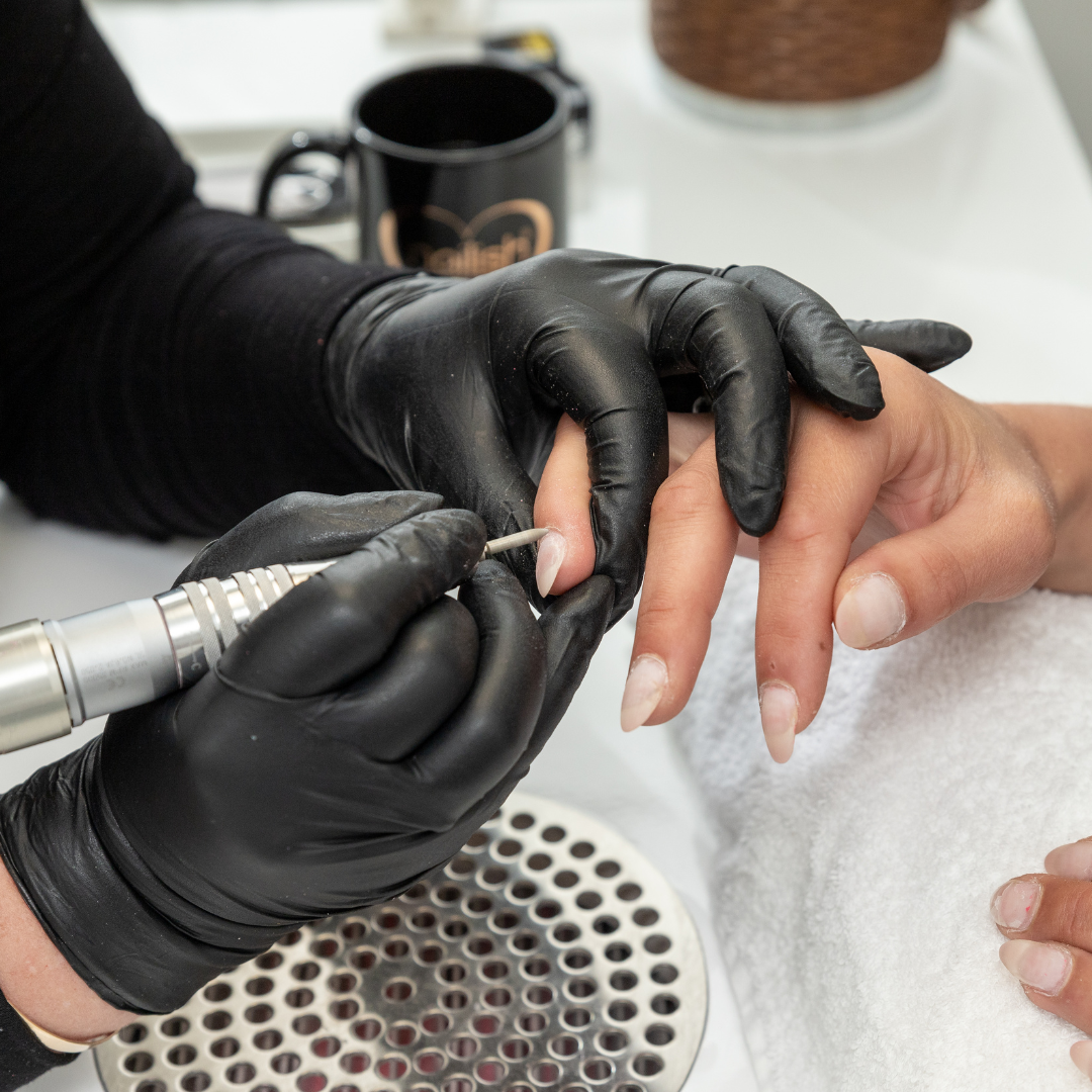 Manicurist using electric nail file to shape client's nails