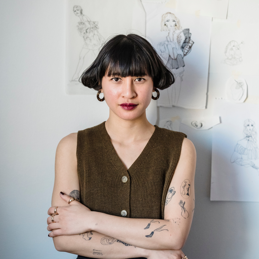 Woman with tattoos near wall with papers with sketches