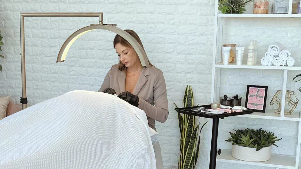 a person performing a cosmetic procedure, likely eyelash extensions or a facial treatment, under a CosmoGlo light