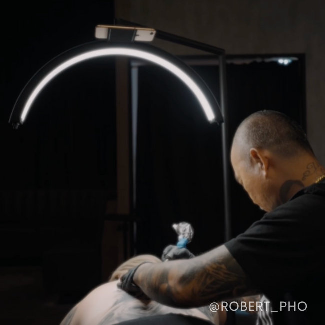 Tattoo artist creating detailed designs under a CosmoGlo daylight lamp.