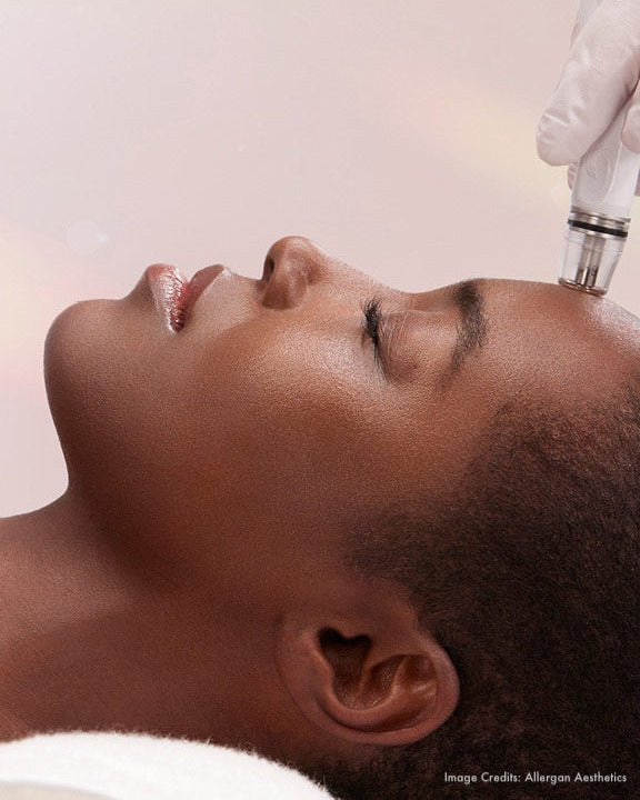 Person receiving a facial treatment with a device on a pink background