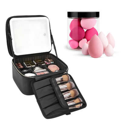 An open black makeup organizer case shown on a white background, with a mirror on the inside lid, makeup items in the main compartment, brush handles in an attached roll-out section, and several pink teardrop makeup sponges displayed beside it in a clear jar.