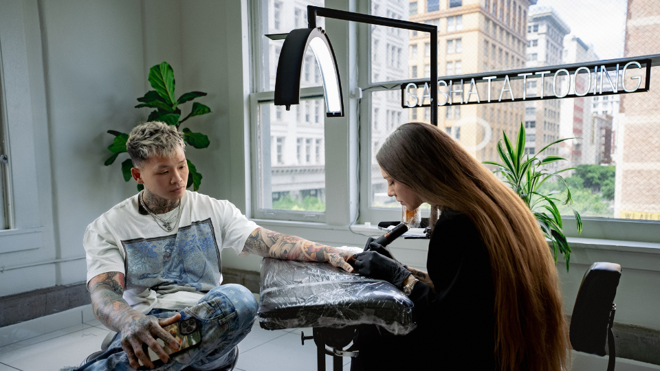 Sasha Tattooing by Sasha Masuik performing a tattoo session underneath the cosmoglo tattoo light made for tattoo artists.