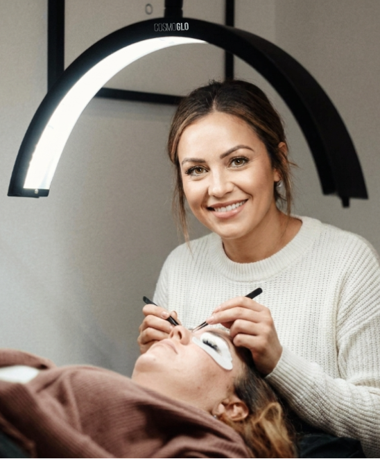 Woman getting eyelash extensions with a professional in a salon setting.