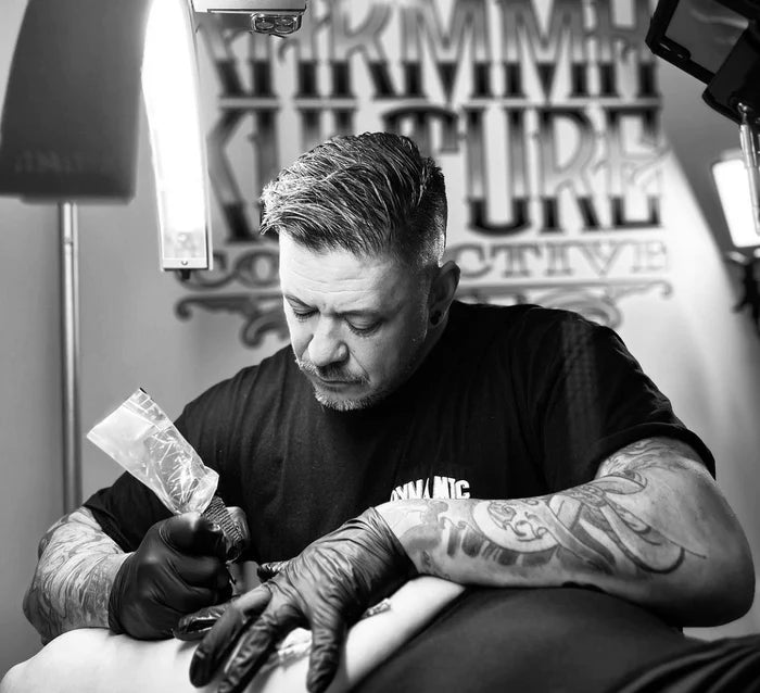 Tattoo artist working on a client's tattoo with precision and focus under bright studio lighting | CosmoGlo Light for Tattoo artist.