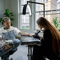 Tattoo artist working on a client's arm in a tattoo studio with cityscape view.
